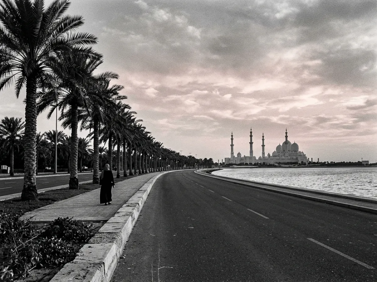Corniche d'Abu Dhabi en fin d'après-midi, palmiers alignés, ligne du golfe, silhouette de la Grande Mosquée qui se découpe en arrière-plan sur un ciel pastel