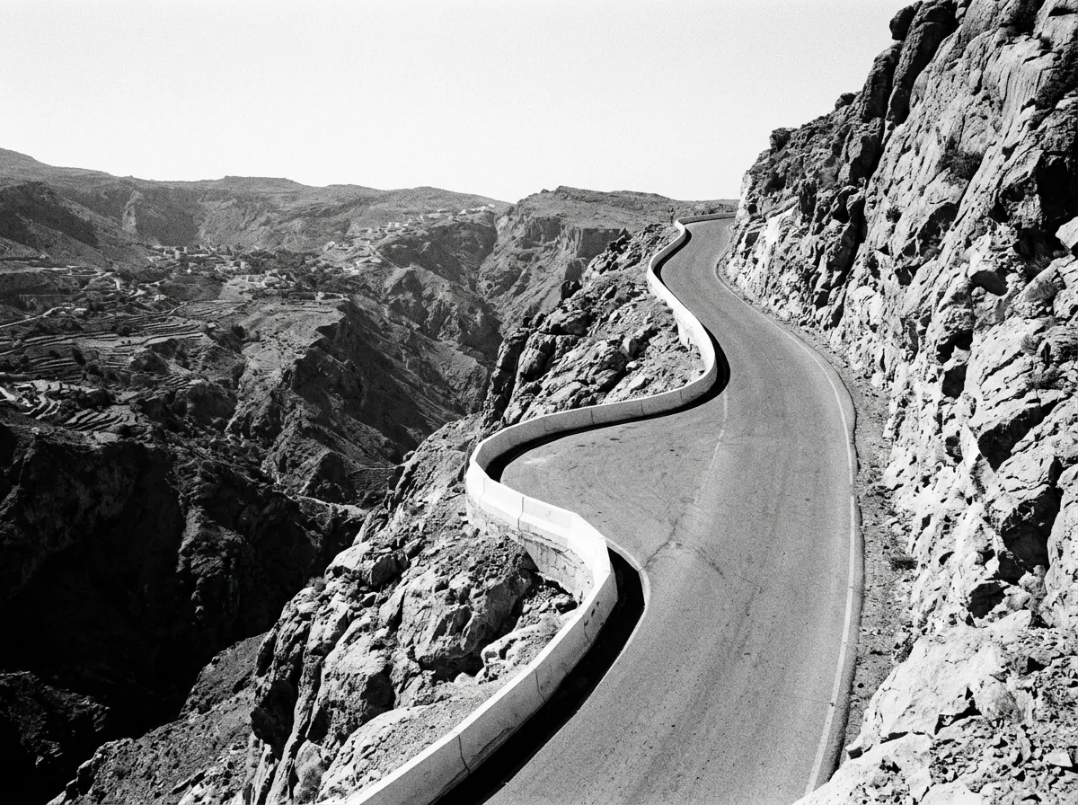 Route en lacets serrés montant vers le plateau de Saiq, barrière blanche de sécurité, virage serré à 15%, falaise à droite, vue plongeante sur la vallée, Jebel Akhdar