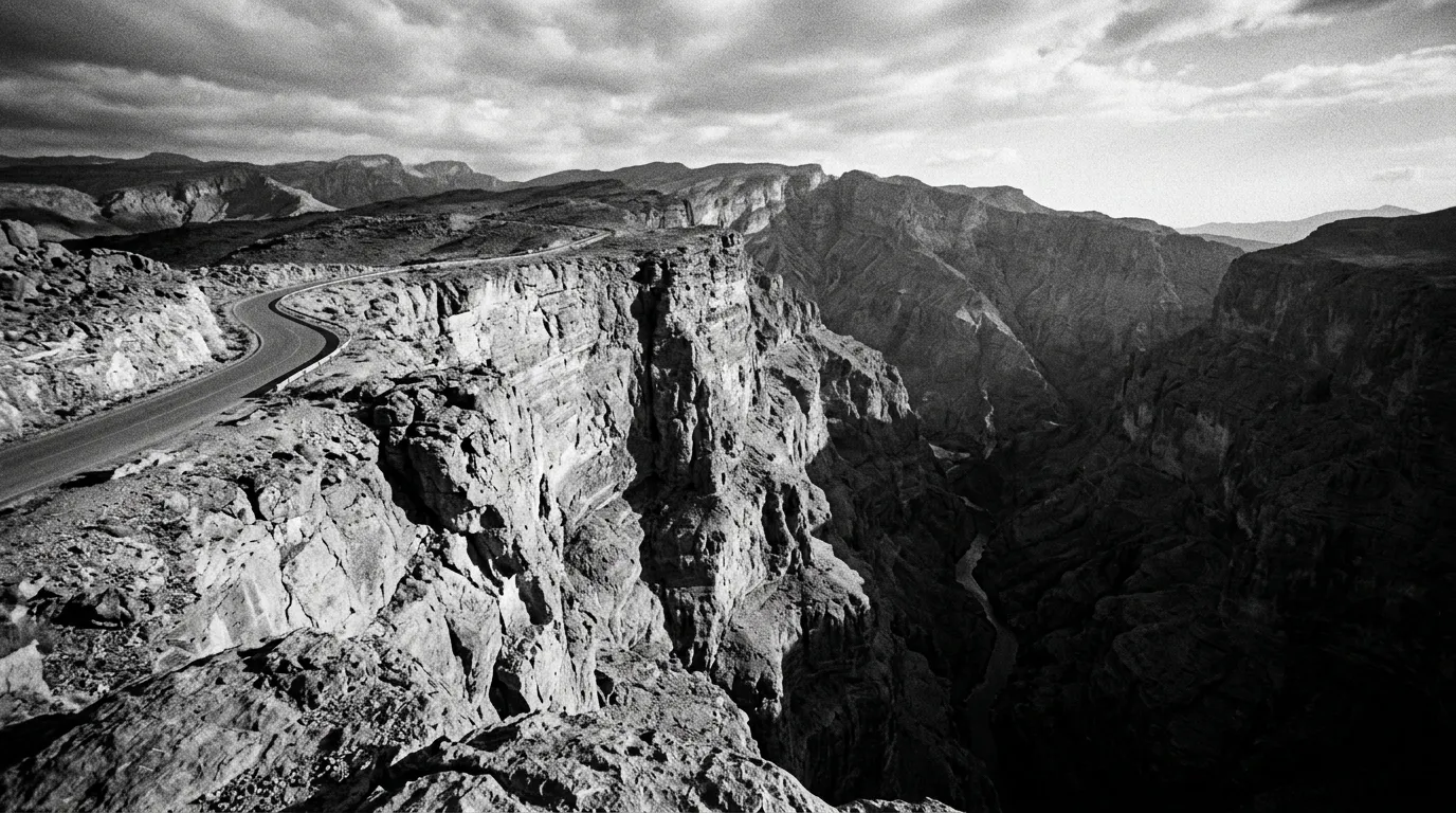Falaise à pic du Grand Canyon de Jebel Shams, aplomb vertical de mille mètres, gouffre d'Al Nakhr au fond, lumière de fin d'après-midi rougeoyante sur la roche, vide spectaculaire