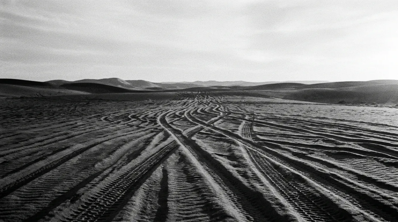 Traces de pneus ondulées sur sable rouge en fin d'après-midi, ombres longues, horizon de dunes jusqu'à l'infini, aucune présence humaine, lumière dorée rasante