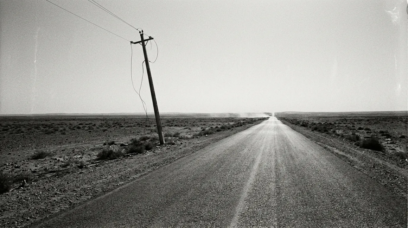 Route rectiligne de la P19 vers Tataouine, mirage de chaleur, horizon vide sous ciel pâle, unique poteau électrique incliné